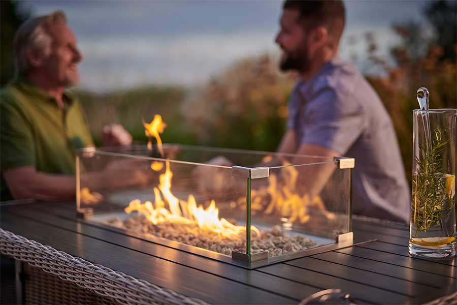 People enjoying an evening in the garden sitting around a kettler Palma dining table with gas fire pit